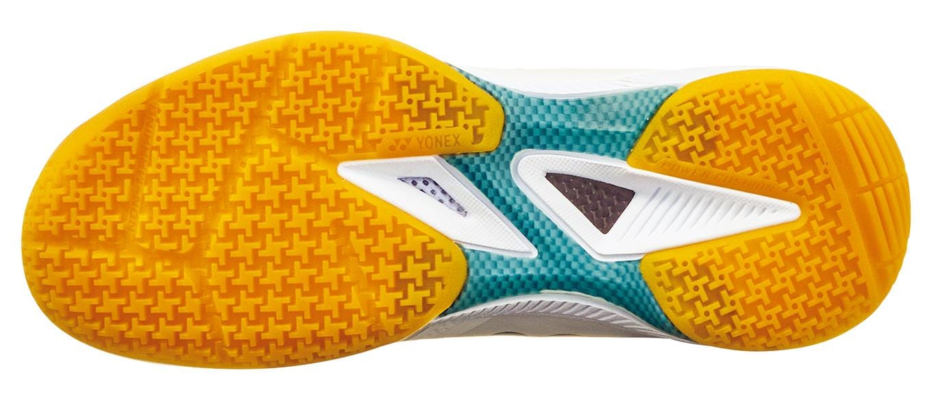 The image shows the yellow, green, and white textured sole of the Yonex Power Cushion 65Z4 Womens Badminton Shoes - White, viewed from the bottom, featuring intricate tread patterns for grip and support.