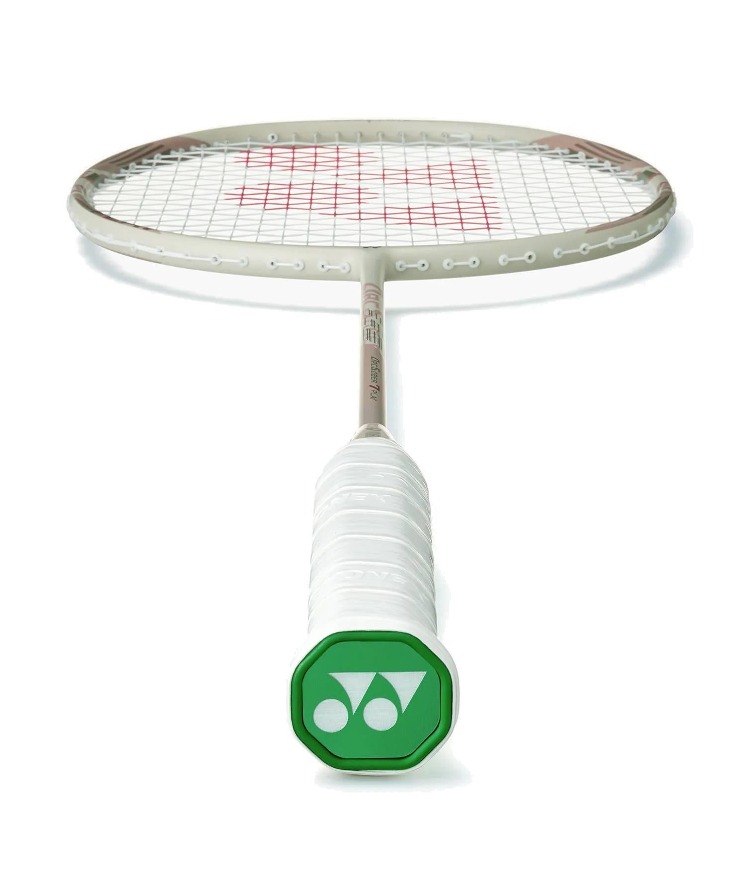 A Yonex Arcsaber 7 Play 4U Badminton Racket - Light Beige is shown lying flat with the handle facing the camera, highlighting its green end cap, white grip, and distinctive ISOMETRIC frame design in the background.
