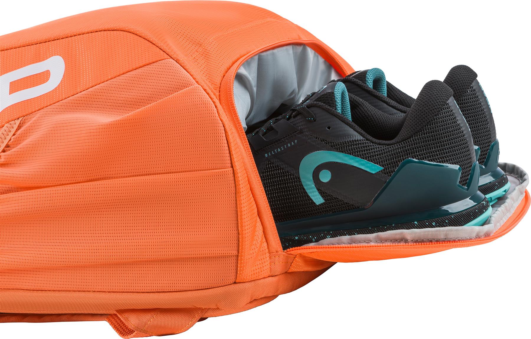 A pair of black and teal athletic shoes are partially inside an open, bright orange HEAD Tour 25L Badminton Backpack by HEAD, with a visible zippered compartment.