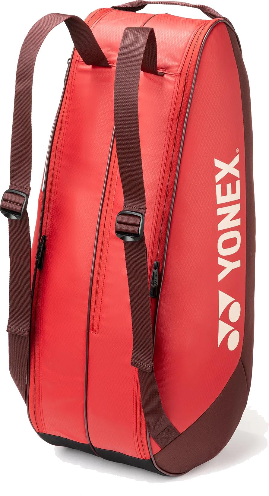 The Yonex 42526EX Team 6 Racket Badminton Bag in ruby red features brown adjustable shoulder straps, two zippered compartments, and a white Yonex logo—ideal for carrying your gear and rackets in style.