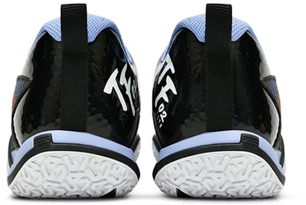 The image displays Li-Ning Saga II Lite Men's Badminton Shoes in black and white. They have a glossy black heel with white text, textured white sole, and upper accents in light blue and black, complete with a back pull tab, blending performance with style effortlessly.