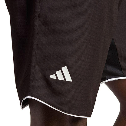 Close-up image of a person wearing the ADIDAS Mens Club 7" Badminton Shorts - Black, featuring a white geometric adidas logo on the side. These shorts incorporate AEROREADY technology and are accented with a white trim along the hem.