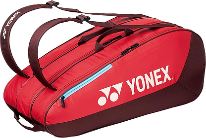 The Yonex 42529EX Team 9 Racket Badminton Bag in Ruby Red features brown handles, black zippers, the white Yonex logo, and multiple compartments for carrying sports gear.
