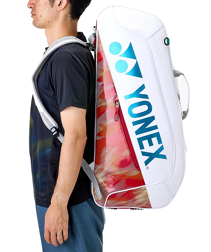 A man in a black shirt and blue shorts carries a Yonex 02626EX Expert 6 Racket Badminton Bag in white with red accents on his back, shown from the side.