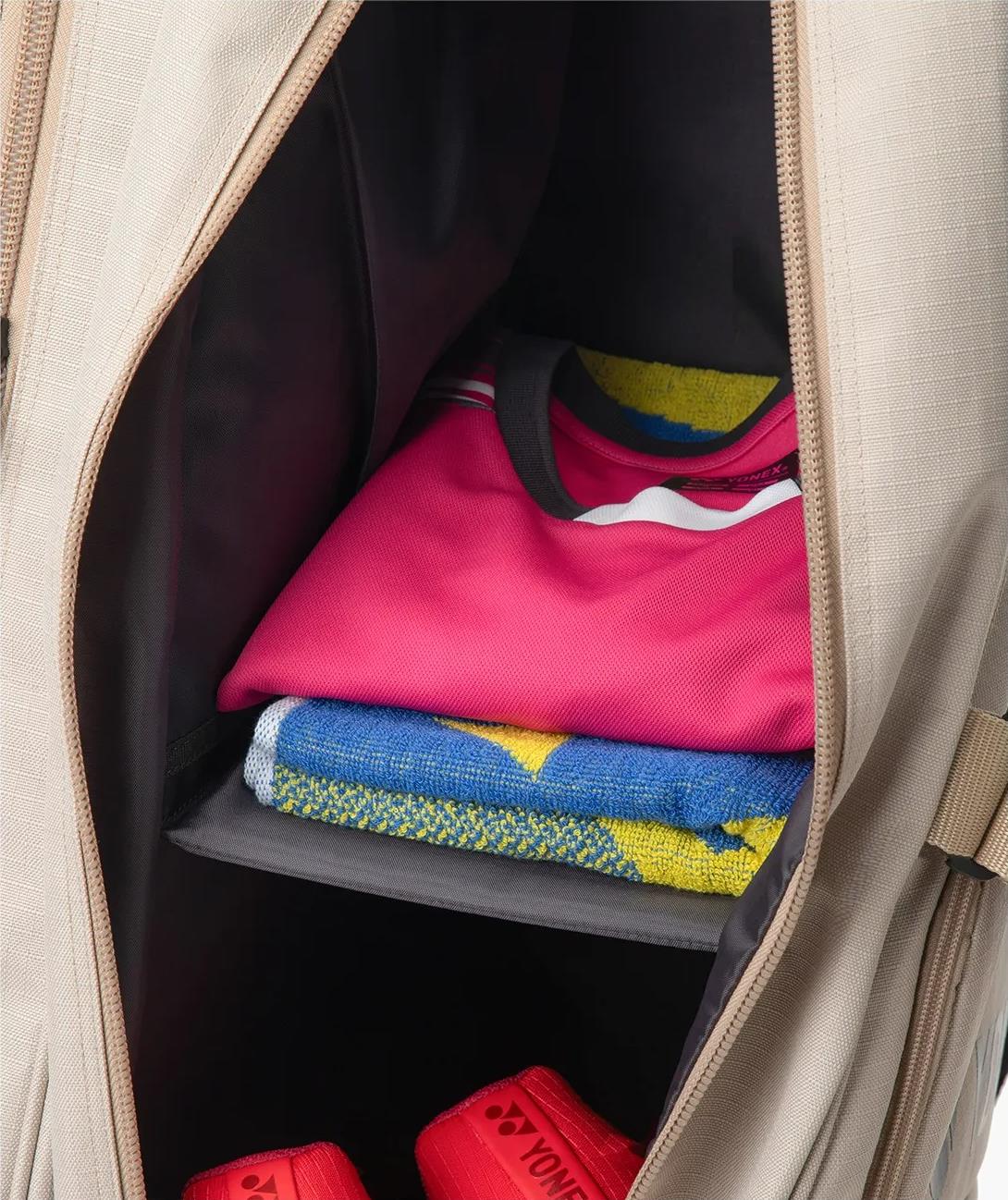 A beige Yonex BA72626EX Gearlogic 6 Racket Badminton Bag made from recycled polyester is shown open, with a folded pink shirt, colorful towel, and red Yonex shoes neatly arranged inside.