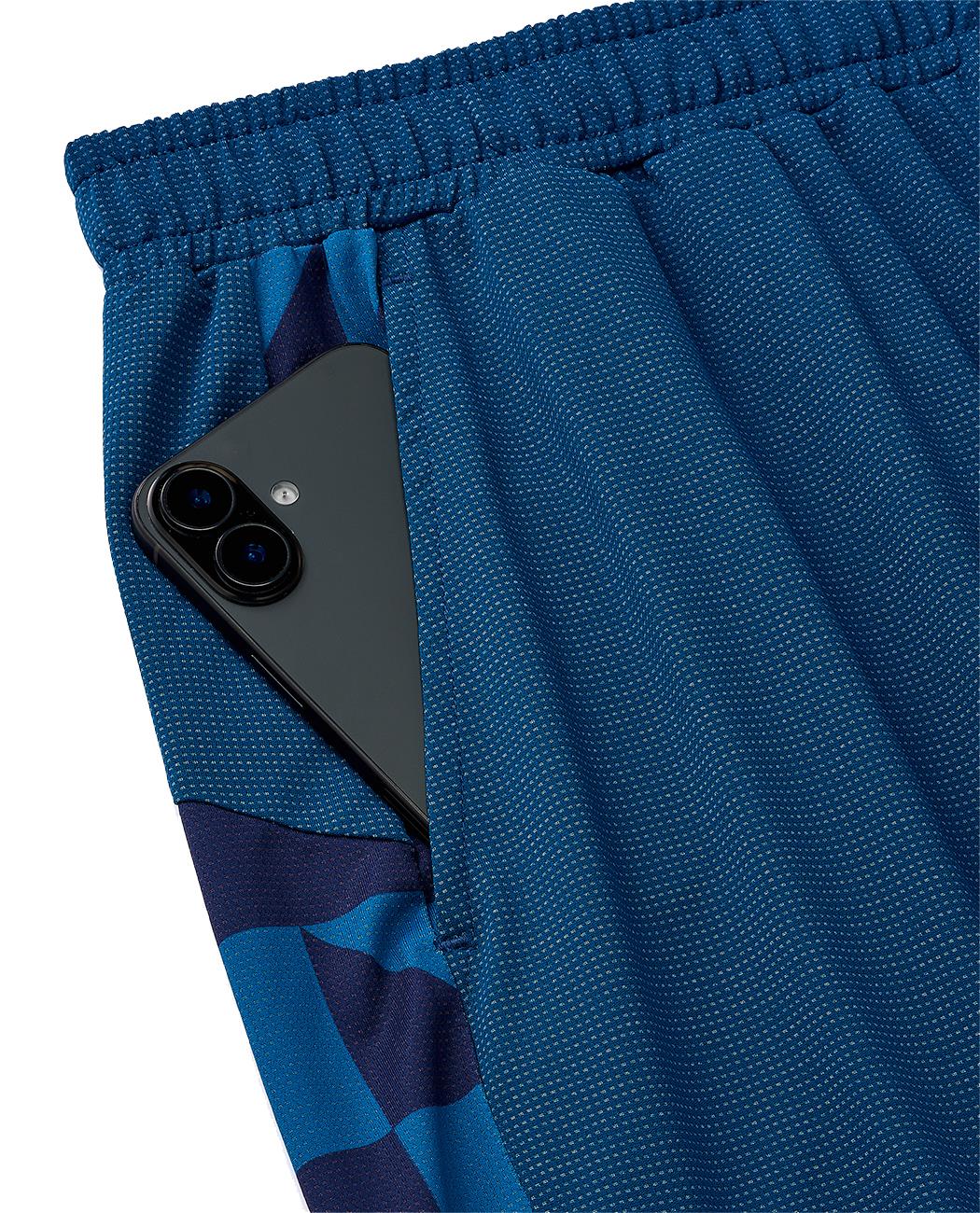 A black smartphone with dual rear cameras is partially tucked into the front pocket of Yonex 15240YX Knit Men's Badminton Shorts in indigo blue, featuring a patterned design.