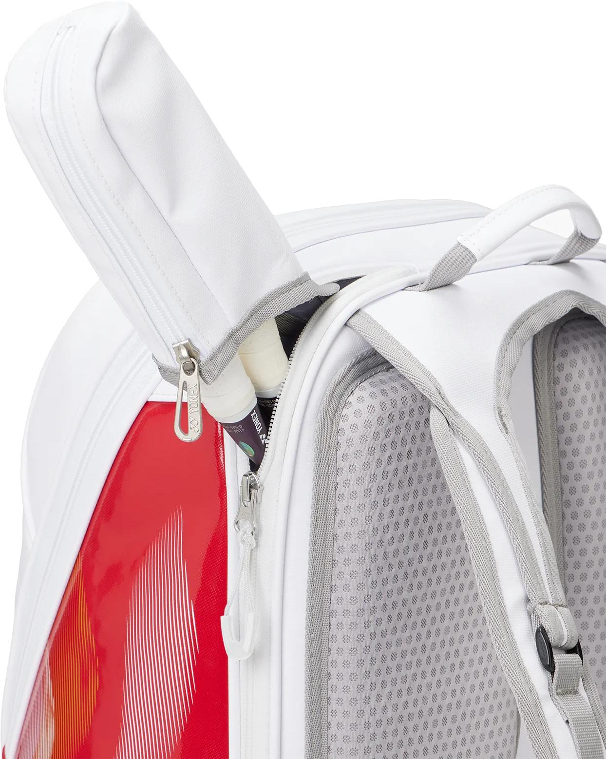 A close-up of the Yonex 02612EX Expert Badminton Backpack - White shows a zippered pocket partially open to reveal two white-handled racquets inside. The Yonex backpack features padded straps and mesh details.