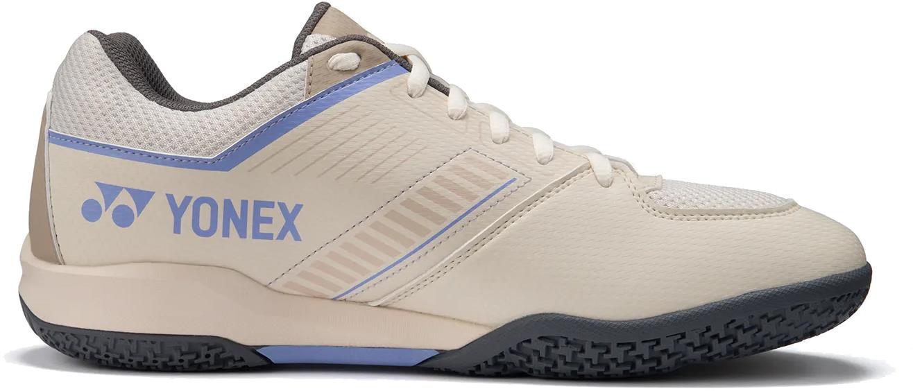 The Yonex Strider Flow WIDE Men's Badminton Shoes in light beige feature blue and grey accents, the Yonex logo on the side, a textured black sole, and white laces—ideal for beginners.