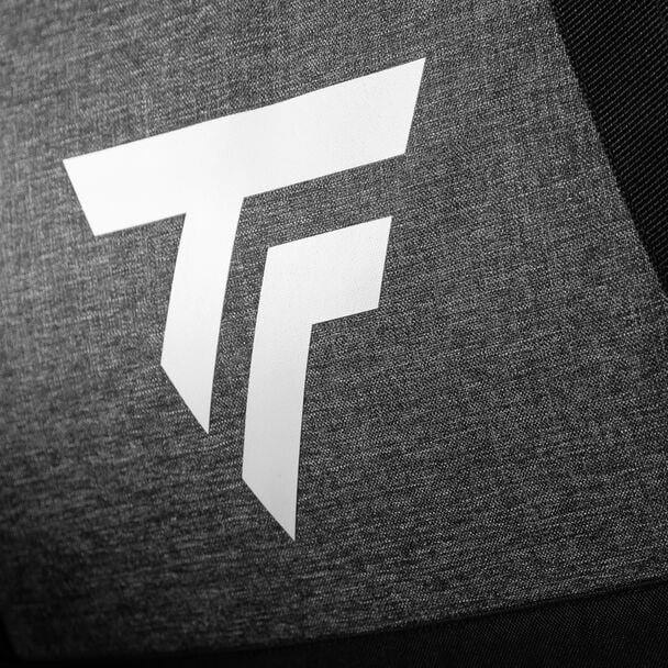 Close-up of a Tecnifibre logo featuring a stylized "T" and "F" in white against a textured dark gray background, evoking the precision associated with racquet sports, as seen on the Tecnifibre All Vision Badminton Duffle Bag - Grey.