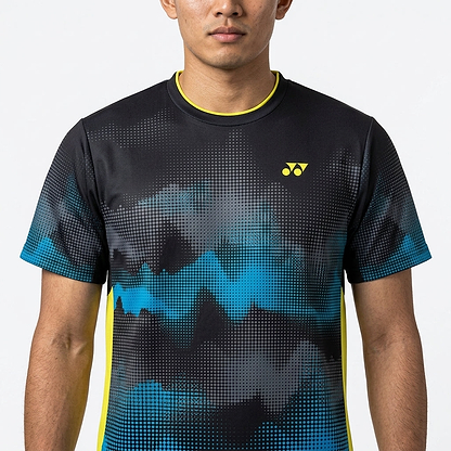 A man faces forward wearing the Yonex YTM2025A Men's Badminton T-Shirt in black, featuring an abstract black and blue design, yellow Yonex logo, quick-dry technology, and yellow trim on the collar and sides. Only his upper body is visible.