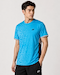 A man wears a Yonex YTM11 Men's Badminton T-Shirt in Blue Sea with a geometric pattern, paired with black shorts, his left hand in his pocket, gazing to the side against a plain light background.
