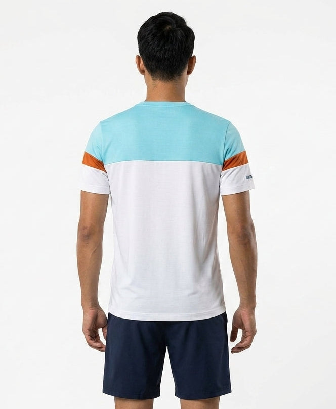 A man, facing away, wears the Babolat Crew Neck Mens Badminton T-Shirt in white by Babolat, featuring a light blue top, orange shoulder stripes, and a white lower section with dark navy shorts against a plain white background.