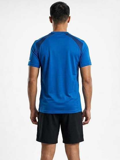 A man faces away from the camera, wearing the Le Coq Sportif Pro Men's Badminton T-Shirt in Lapis Blue with black shorts—breathable Le Coq Sportif sportswear set against a plain white background.