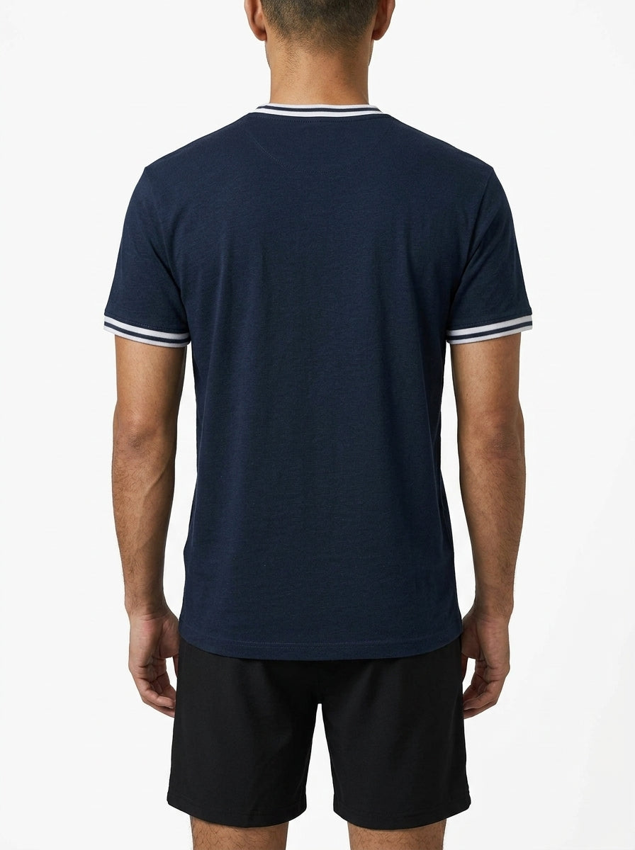 A man stands with his back to the camera, wearing a Tecnifibre Team Stretch Mens Badminton T-Shirt in marine blue with white trim and black shorts, set against a plain white background.