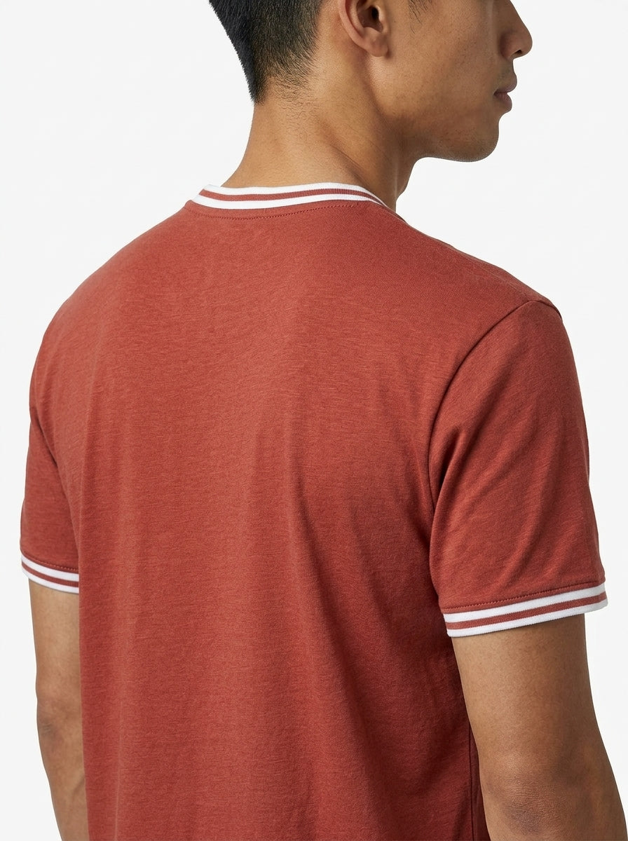 A man is seen from behind wearing a Tecnifibre Team Stretch Mens Badminton T-Shirt in terracotta, featuring white-striped trim on the collar and sleeves, set against a plain white background.