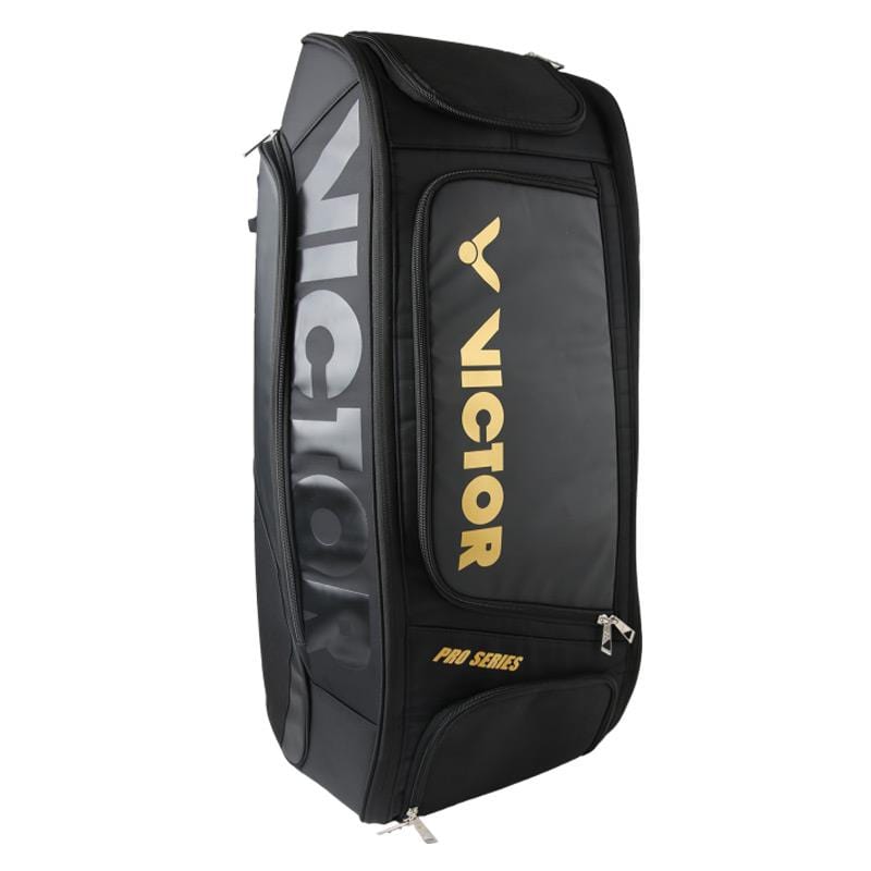 The Victor Rucksack BR7007 C Badminton Bag in black and gold is designed to stand upright, featuring multiple zippered compartments, a designated shoe compartment, and a shoulder strap, making it perfect for organizing your gear.