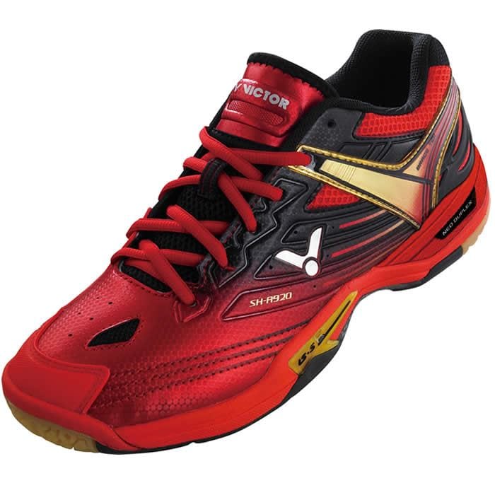 Introducing the Victor SH A920 Red Badminton Shoes: These vibrant red shoes, accented with black and gold, are specifically designed for badminton players. They boast intricate detailing, feature breathable mesh uppers, reliable lateral support, and cushioned soles for optimal performance. Complete with red laces for a secure fit, they are perfect for indoor sports and active wear.