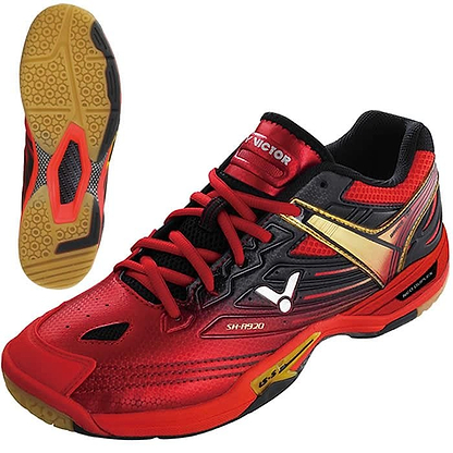The Victor SH A920 Red Badminton Shoes by Victor feature a striking red and black color scheme with a gold accent and black laces. These shoes offer lateral support, and their sole combines yellow and black patterns for an excellent grip, ideal for indoor sports. With its sleek, modern design, these shoes are perfect for the dynamic movements of a badminton player.