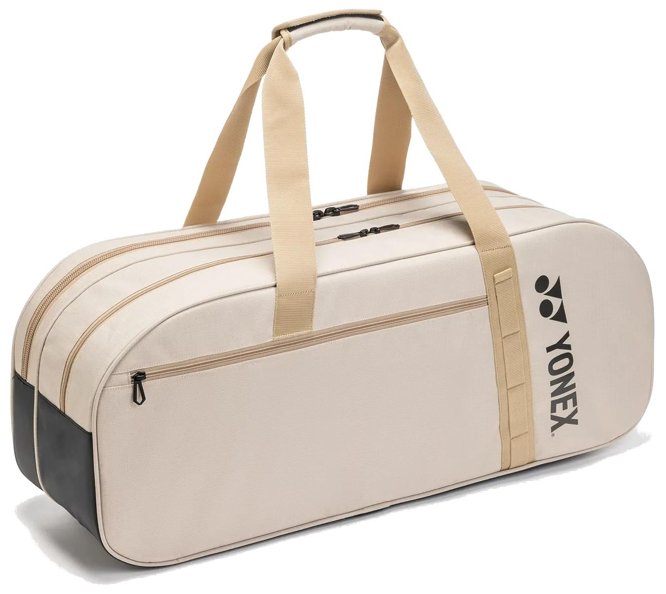 The Yonex BA72631WEX Gearlogic Tournament Badminton Bag in beige features tan handles, black ends, a side pocket with a black Yonex logo, and multiple zippered compartments—ideal for tournaments.