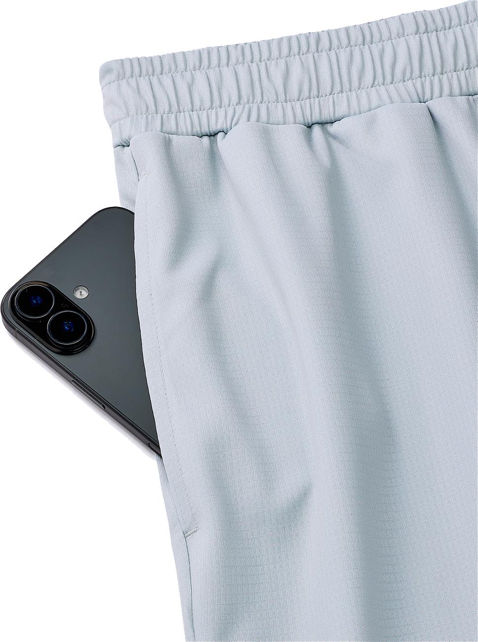 A black smartphone is partially tucked into the side pocket of light grey Yonex 15241EX Knit Men's Badminton Shorts by Yonex, featuring an elastic waistband.