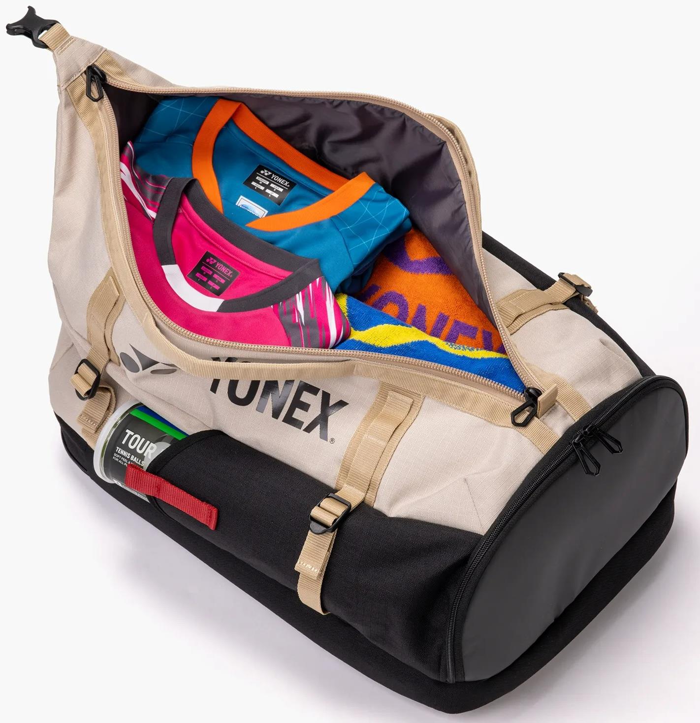 The Yonex BA72612EX Gearlogic Badminton Backpack in beige is shown unzipped, revealing colorful shirts and an orange-blue towel inside. This 40L Yonex bag features sturdy straps, buckles, and branded tags on the exterior.