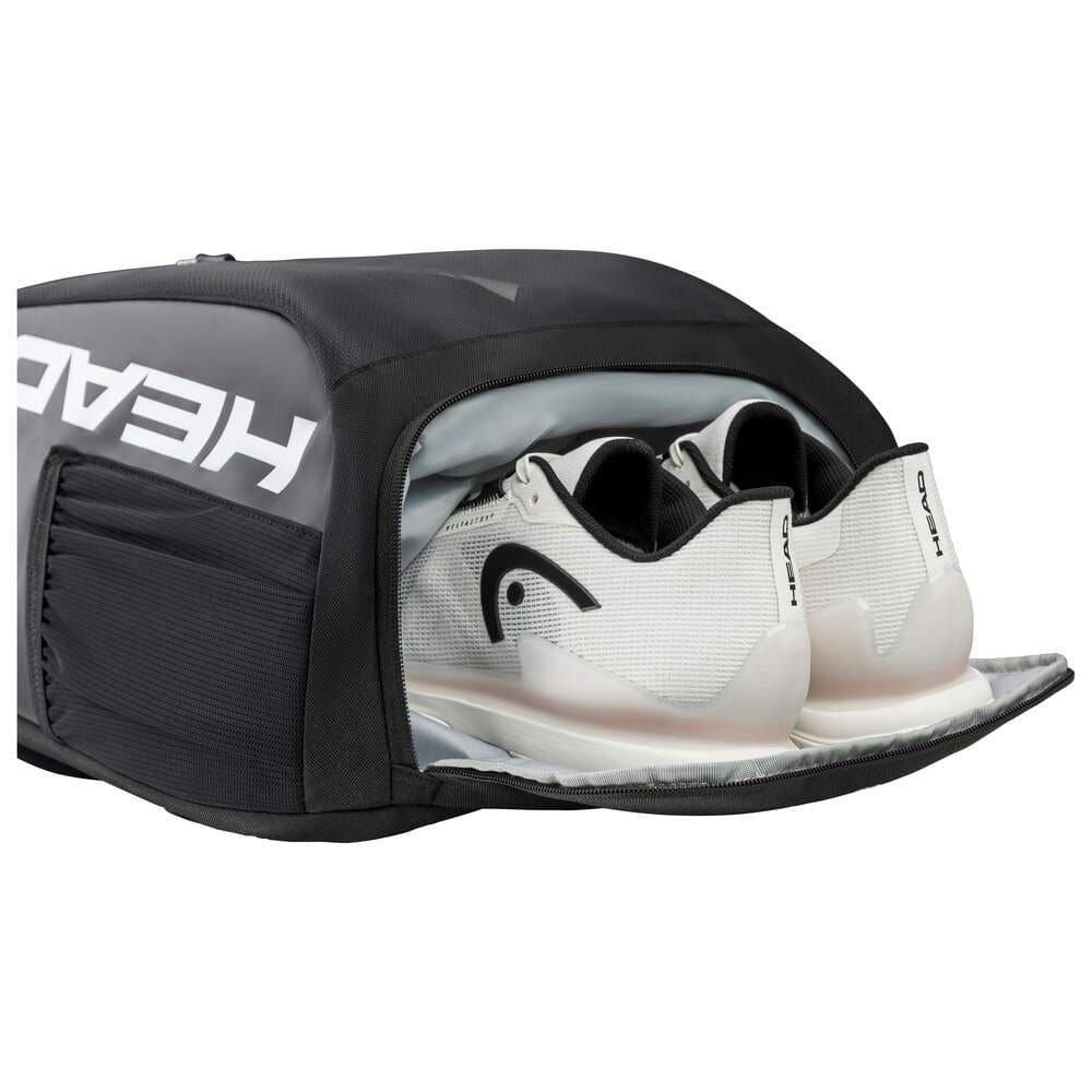 A black sports bag with a shoe compartment is open, showing white athletic shoes inside. The bag, marked with "HEAD" in bold white letters, resembles the HEAD Tour Badminton Backpack - Black / White, known for its generous space for gear and a dedicated racket compartment.