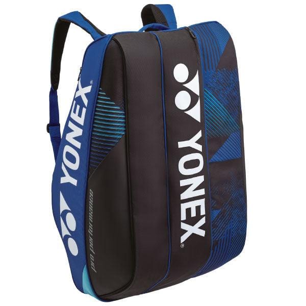 The Yonex 924212EX Pro 12 Racket Badminton Bag in cobalt blue features white branding along with padded shoulder straps, zipper compartments, and geometric patterns on the sides. It includes thermo-guard compartments and can hold up to 12 rackets for optimal storage.