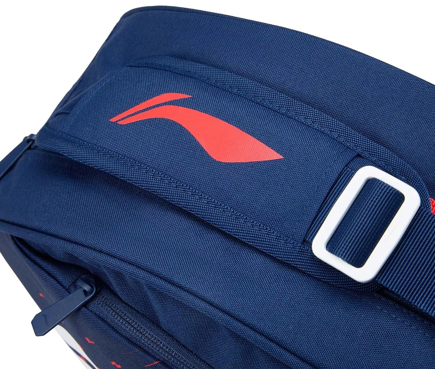 Close-up of the Li-Ning Training Series 3 Racket Badminton Bag in blue/red, featuring a red Li-Ning logo, white buckle on the strap, and a zippered pocket in the lower left for racket accessories.