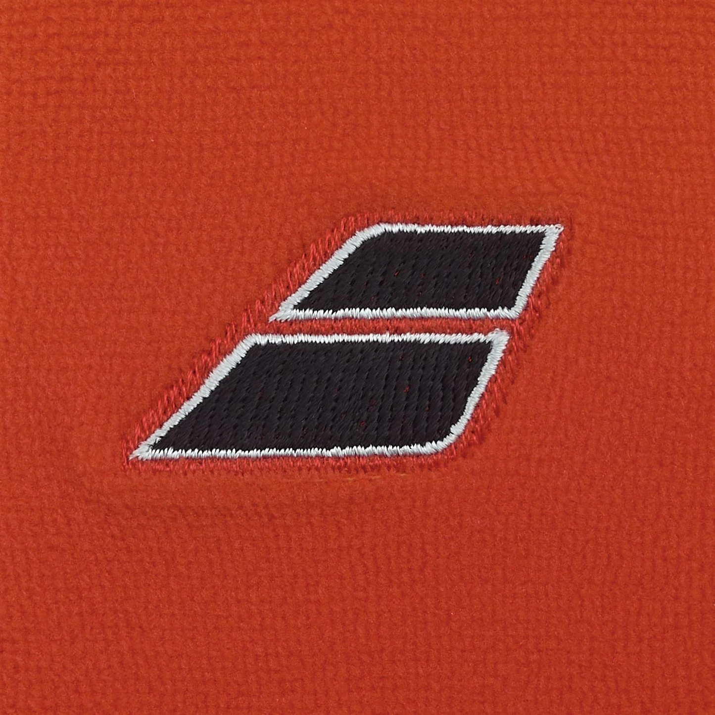 A close-up of Babolat Terry Jumbo Wristband - Cherry Tomato shows textured orange fabric and an embroidered black and white parallelogram logo, making it the perfect sweat-absorbing accessory for tennis enthusiasts.