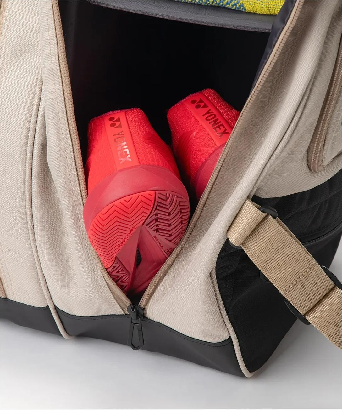 A beige Yonex BA72626EX Gearlogic 6 Racket Badminton Bag, made from recycled polyester, is partially unzipped to display red Yonex athletic shoes organized in a separate compartment.