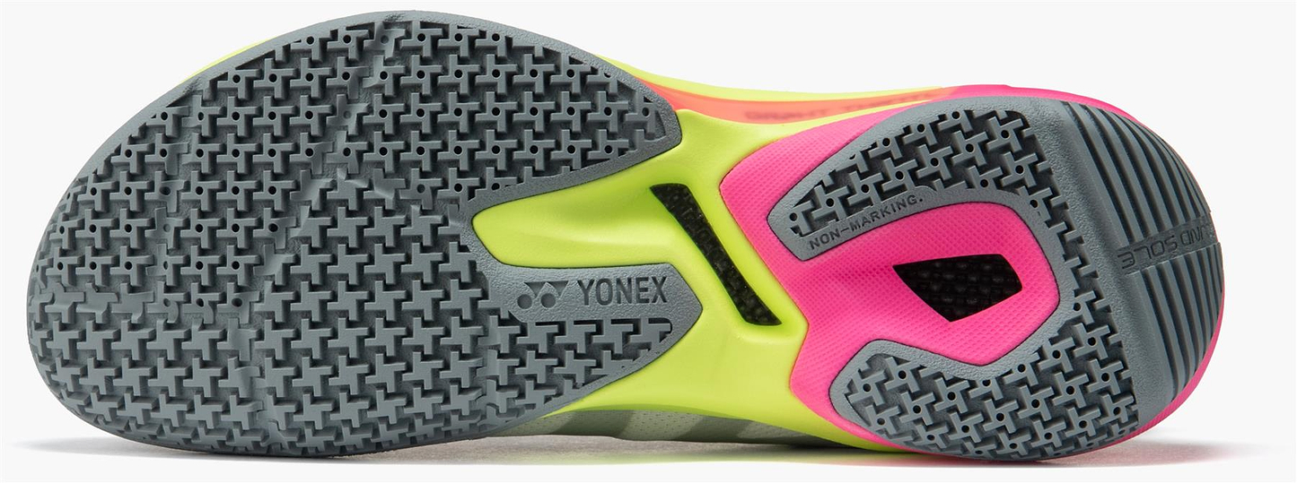 Close-up of the Yonex Subaxia GT Womens Badminton Shoes in Light Grey, highlighting the textured grey sole, yellow-green midsole, pink accents, and GRPHT THRTTL tech for non-marking grip on indoor courts.