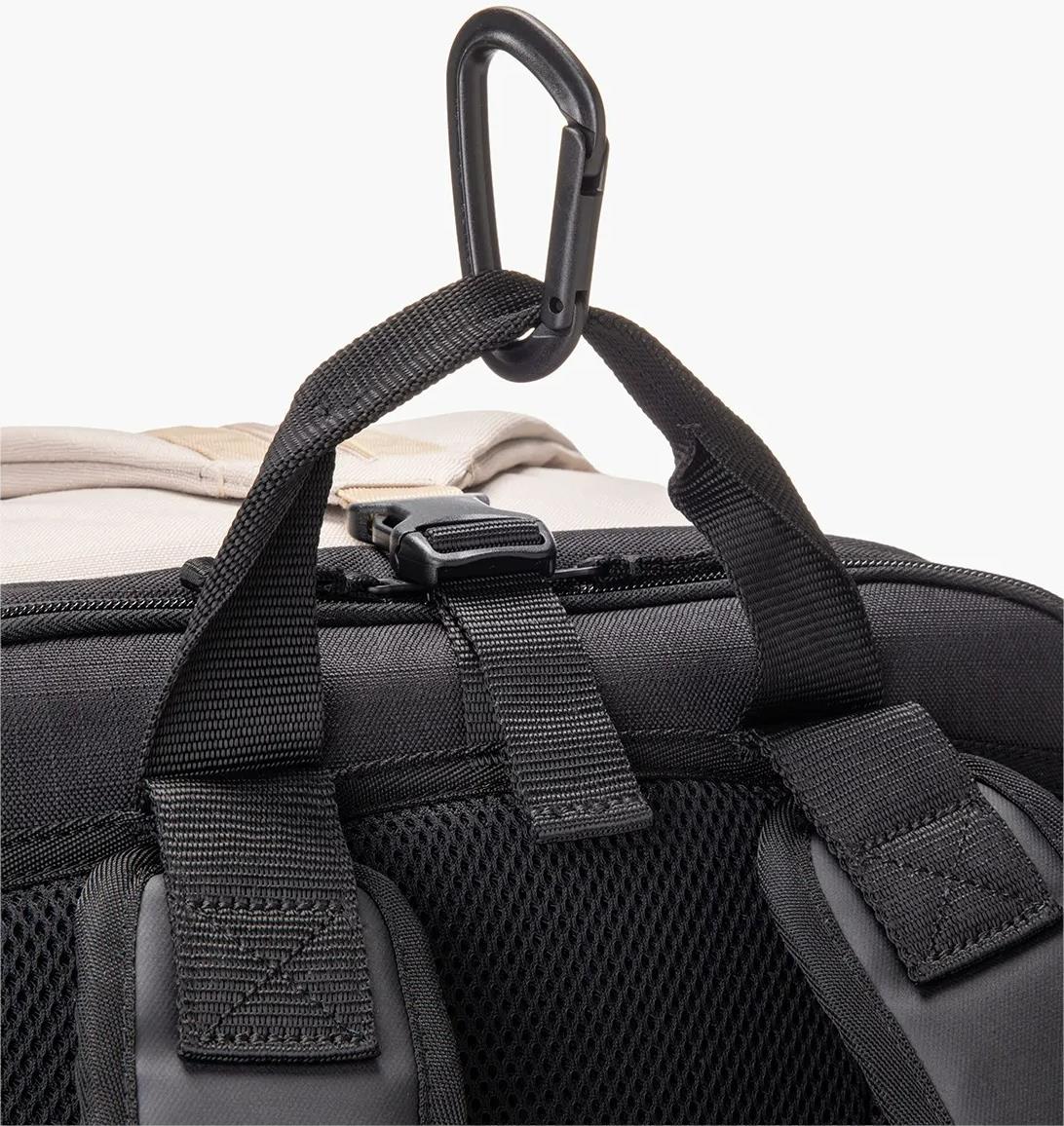 Close-up of the Yonex BA72612EX Gearlogic Badminton Backpack in beige, featuring padded shoulder straps, mesh back padding, a top carrying handle, and a black plastic carabiner attached to an upper loop.
