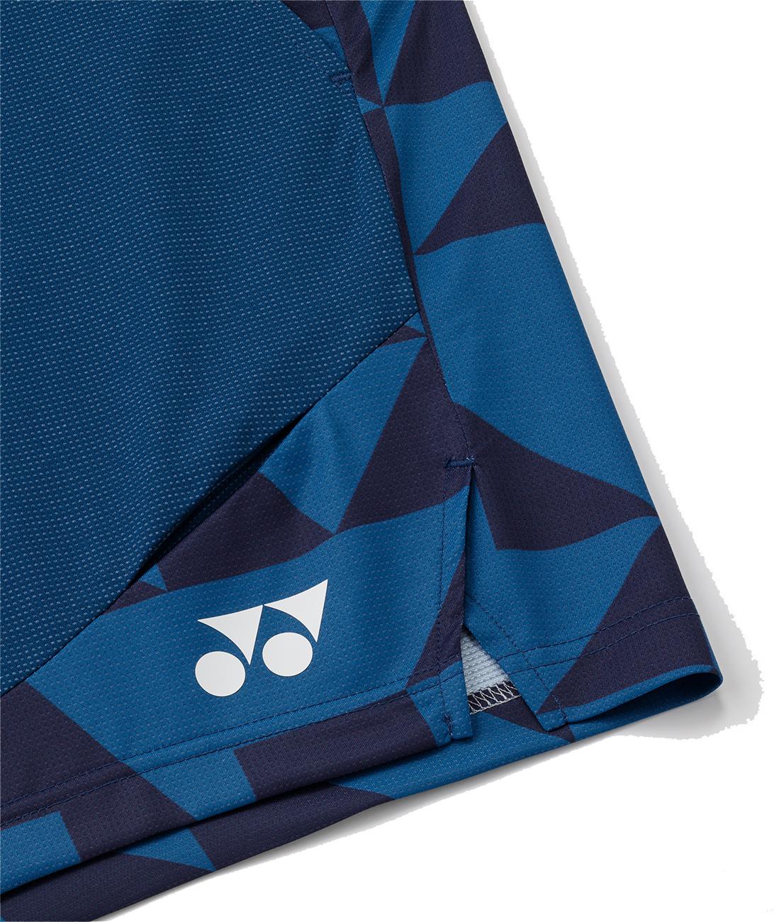 Close-up of the bottom hem of Yonex 15240YX Knit Men's Badminton Shorts in indigo blue, showing a geometric pattern and a white Yonex logo near the edge.