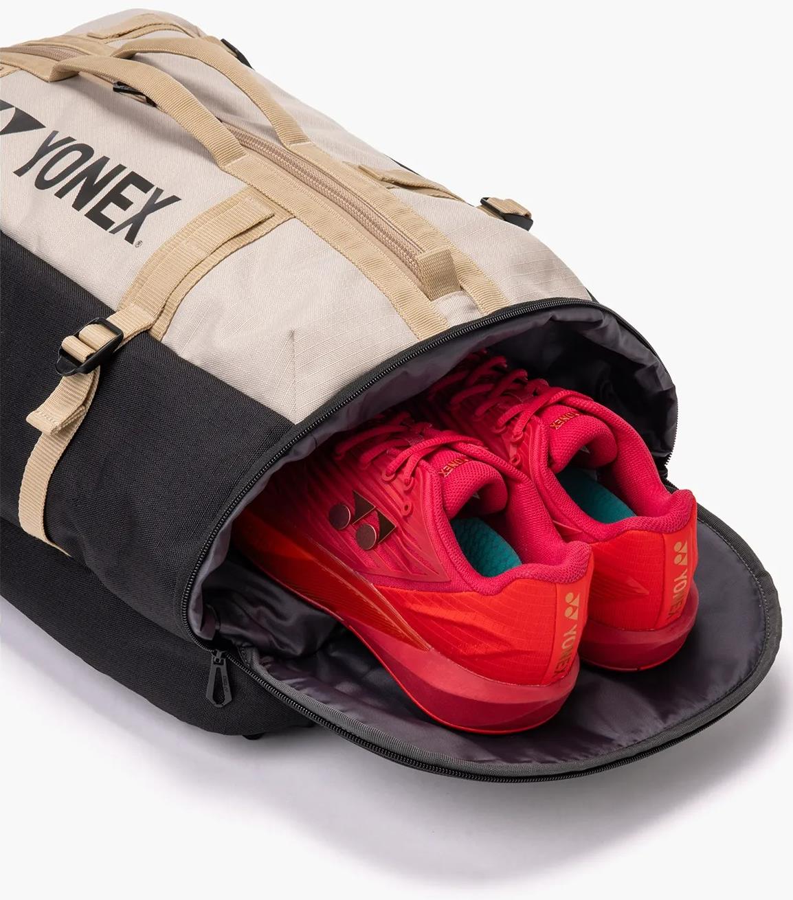 A Yonex BA72612EX Gearlogic Badminton Backpack in beige features a zippered compartment revealing bright red athletic shoes stored neatly, making it the perfect companion for organized sports storage.