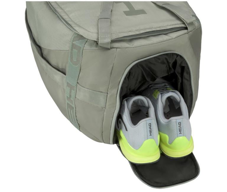 A gray HEAD Pro Duffle Bag M - LNLL includes a shoe compartment holding a pair of gray and neon green athletic shoes partially inside. This bag, with its convenient side handles, offers plenty of space and is ideal for sports or travel, similar to the practical choice favored by Matteo Berrettini.