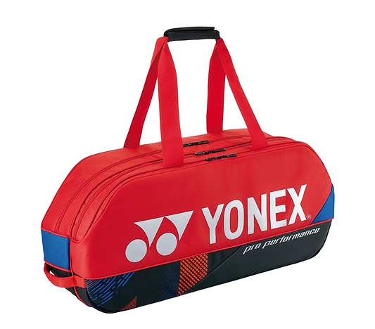 The Yonex 92431WEX Pro Tournament 6 Racket Badminton Bag in Scarlet is equipped with dual handles and a zippered top featuring durable YKK zippers. The bag prominently displays the Yonex logo along with "pro performance" text in white, complemented by sleek black and blue accents on the sides.