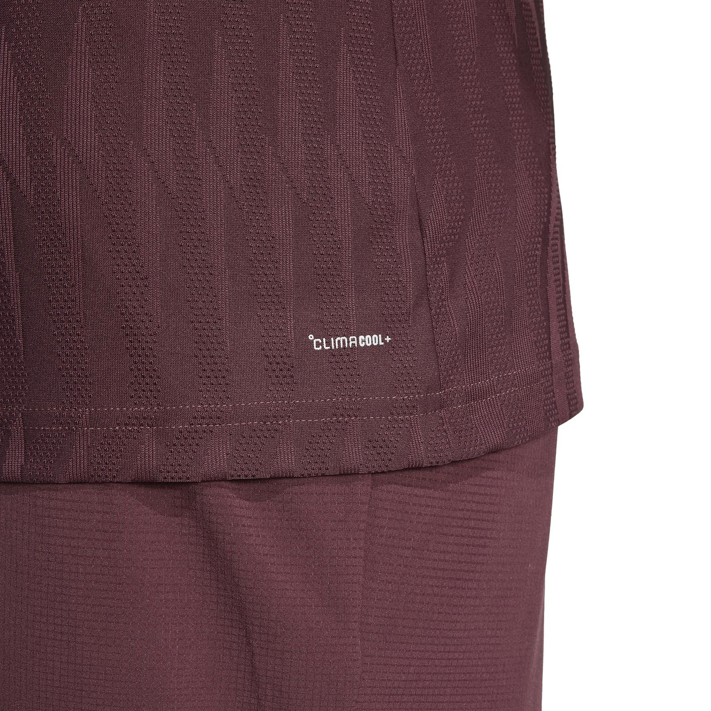 Close-up of the ADIDAS Men's Climacool+ Freelift Badminton T-Shirt in Ruby by adidas, showing a textured geometric design made from recycled materials. The image includes the lower shirt and shorts.