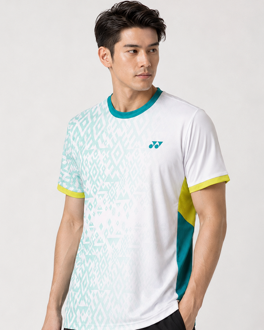 A man with short dark hair wears the Yonex YTM11 Mens Badminton T-Shirt - White by Yonex, which has light green geometric patterns, teal and yellow accents, Air-Release fabric, and a small chest logo, standing against a plain light background.