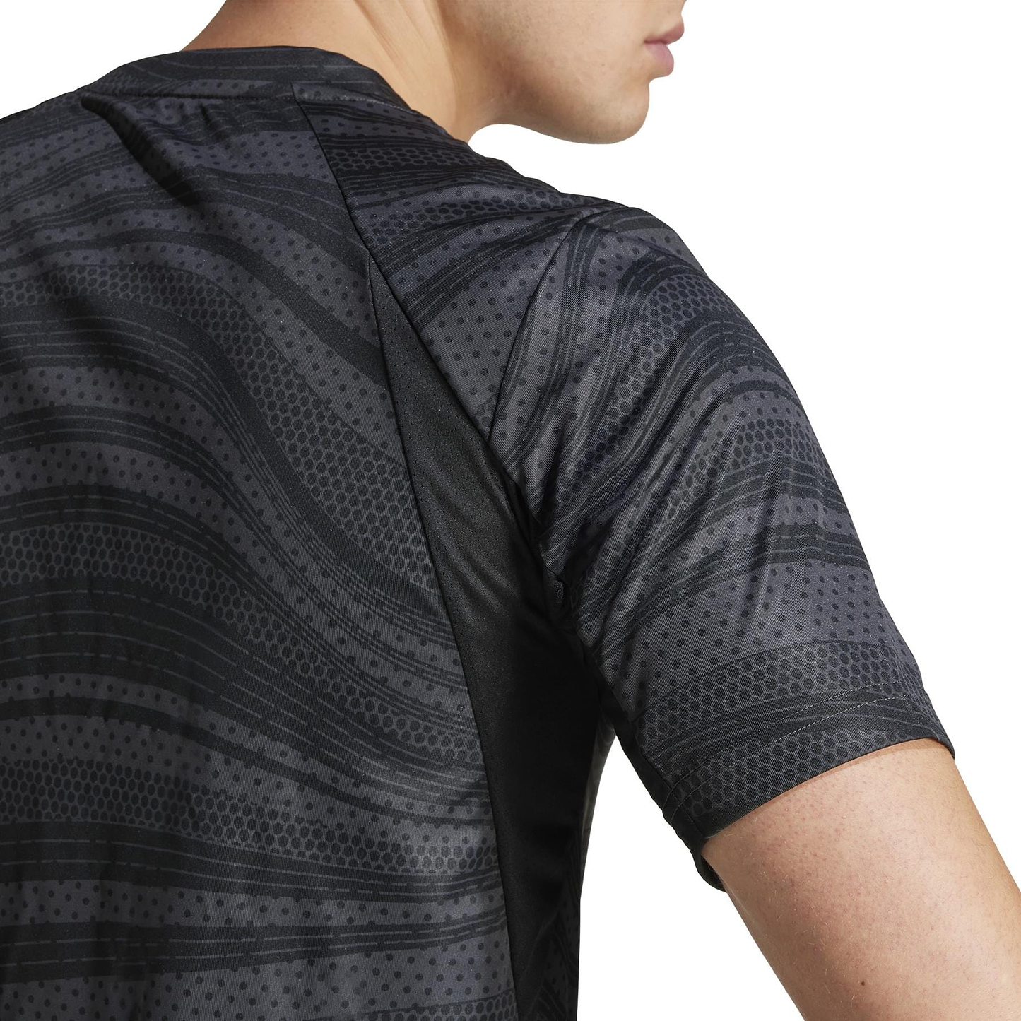 A person is wearing an adidas Club Men's Graphic Badminton T-Shirt in black, made from recycled materials. The shirt has a wavy, dotted design with short sleeves, showcasing style and sustainability from the side view of the upper back and part of the arm.