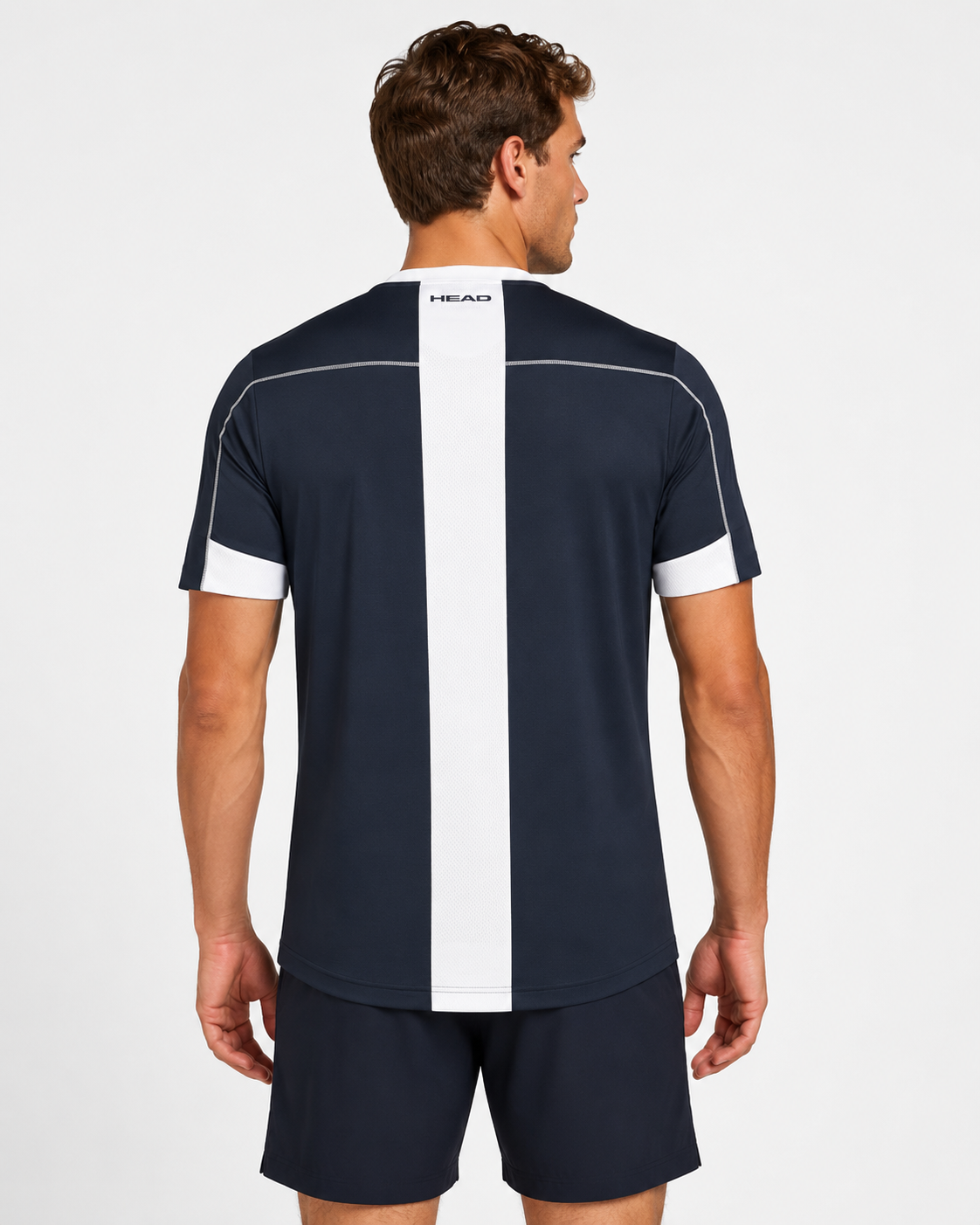 A man, seen from behind in a plain setting, wears the HEAD Play Tech Mens Badminton T-Shirt - Navy by HEAD with a white vertical stripe and moisture transfer microfiber, paired with navy shorts.