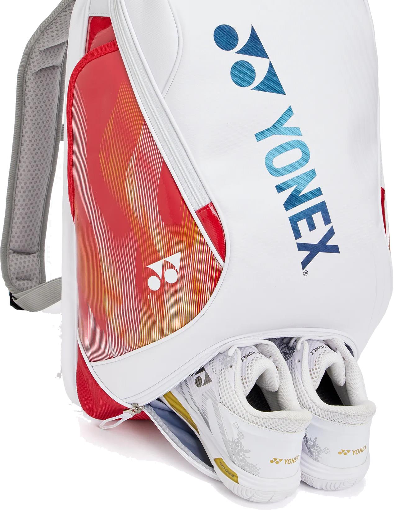 The Yonex 02612EX Expert Badminton Backpack in white features red and orange accents and a blue Yonex logo, with a pair of white Yonex shoes partially visible in the lower compartment.