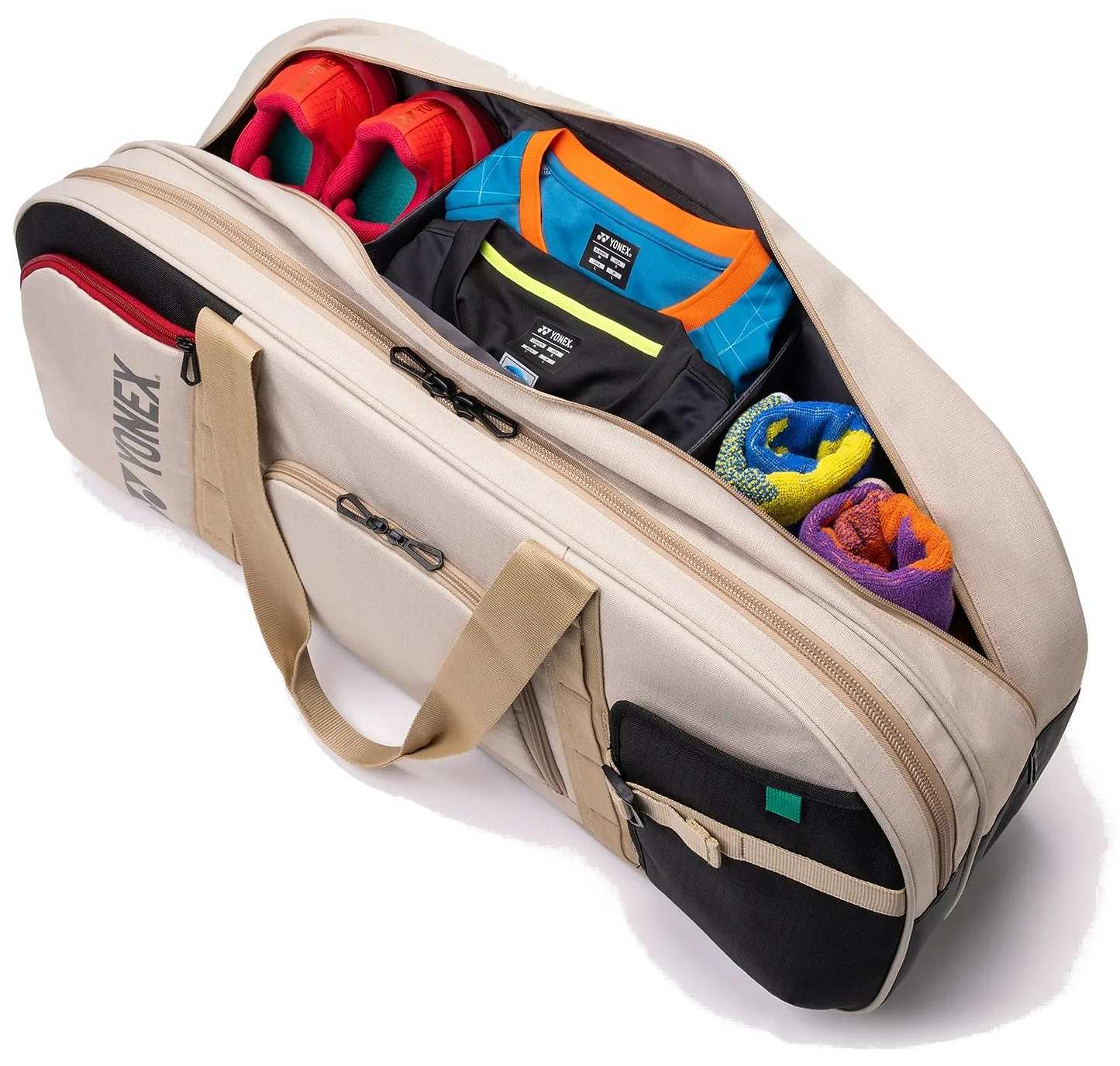 A beige Yonex BA72631WEX Gearlogic Tournament Badminton Bag is open, showing neatly packed clothes, two rolled towels, t-shirts, and a pair of bright red athletic shoes inside.