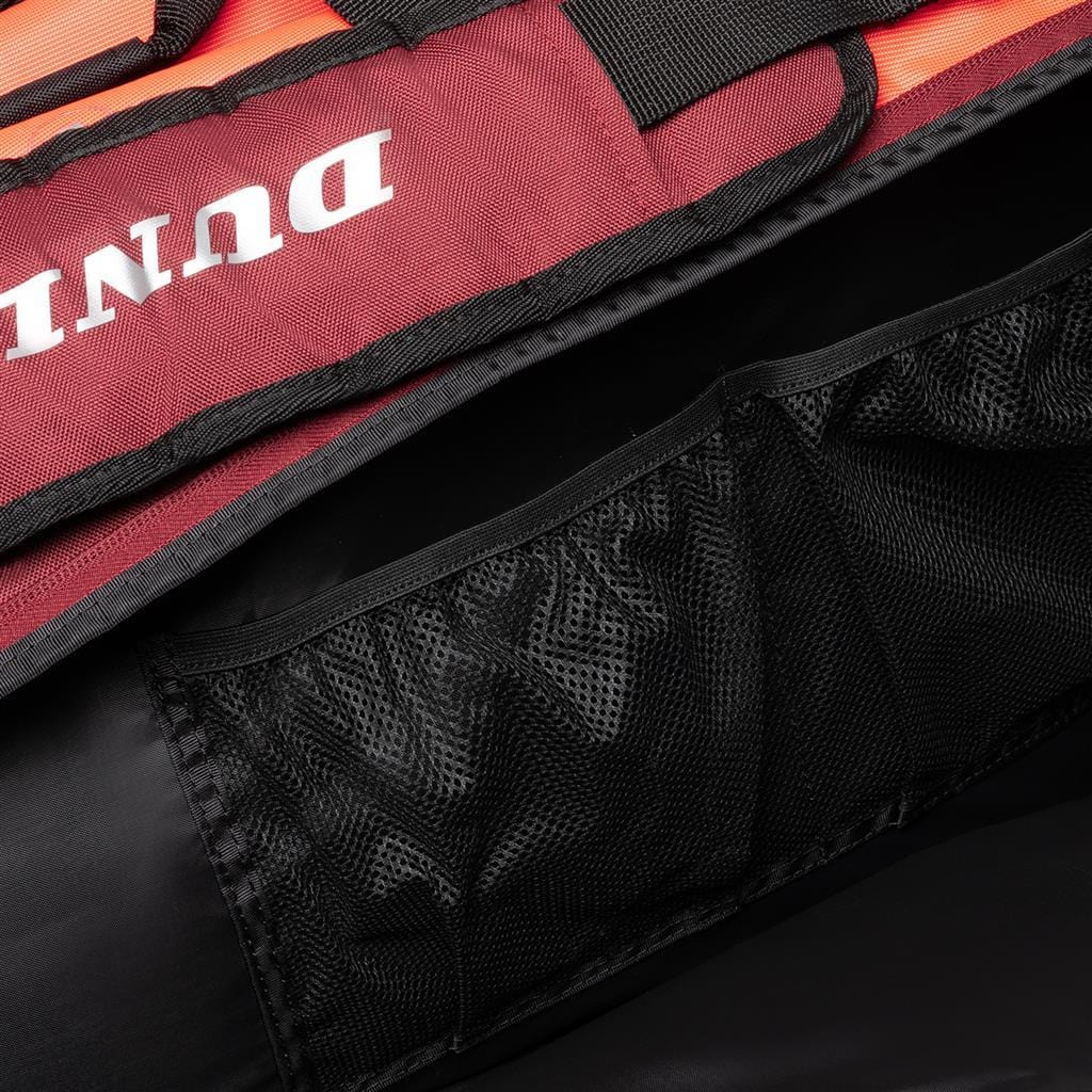 This close-up of the Dunlop CX Performance 12 Badminton Racket Bag showcases its red and black padded design, complete with a visible mesh pocket. The word "DUN" partially appears in white on the fabric, emphasizing its sporty appeal. Ergonomic shoulder straps provide comfort during transport.