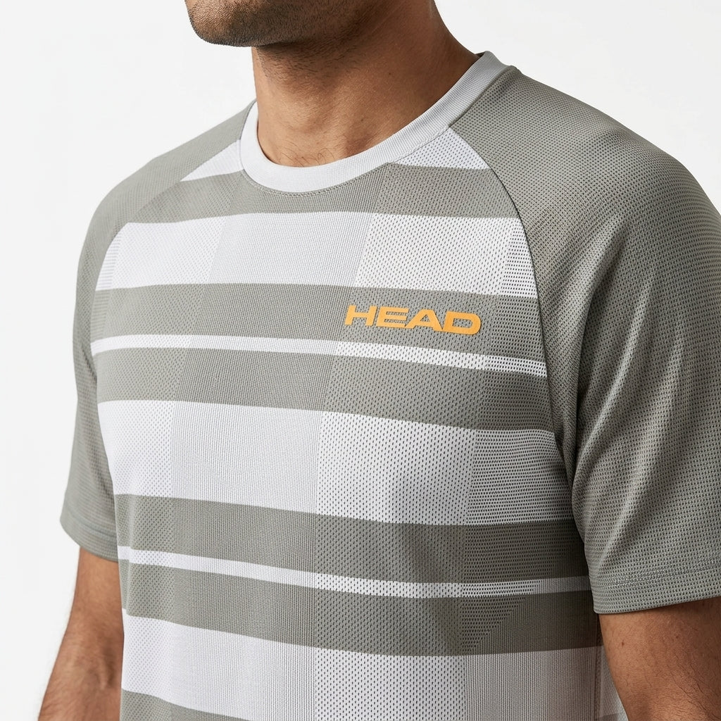 A man wears the HEAD Performance Mens Badminton T-Shirt - XPWG, featuring gray and white stripes, moisture-wicking fabric, and an orange HEAD logo on the left chest, shown from shoulders to mid-torso against a plain background.