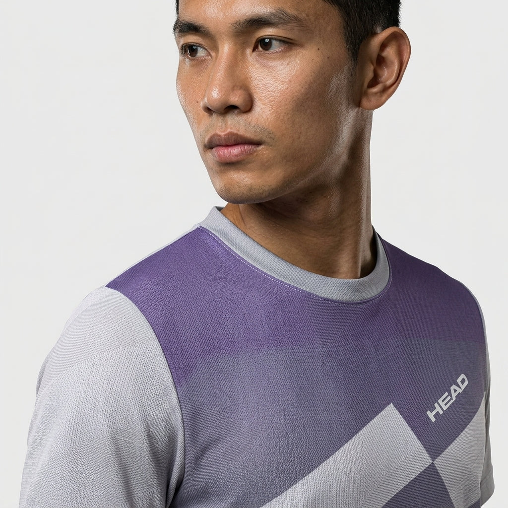 A man with short dark hair wears a HEAD Pro Mens Badminton T-Shirt - PUXP, a purple and gray performance shirt from HEAD, and looks to the side against a plain light background.