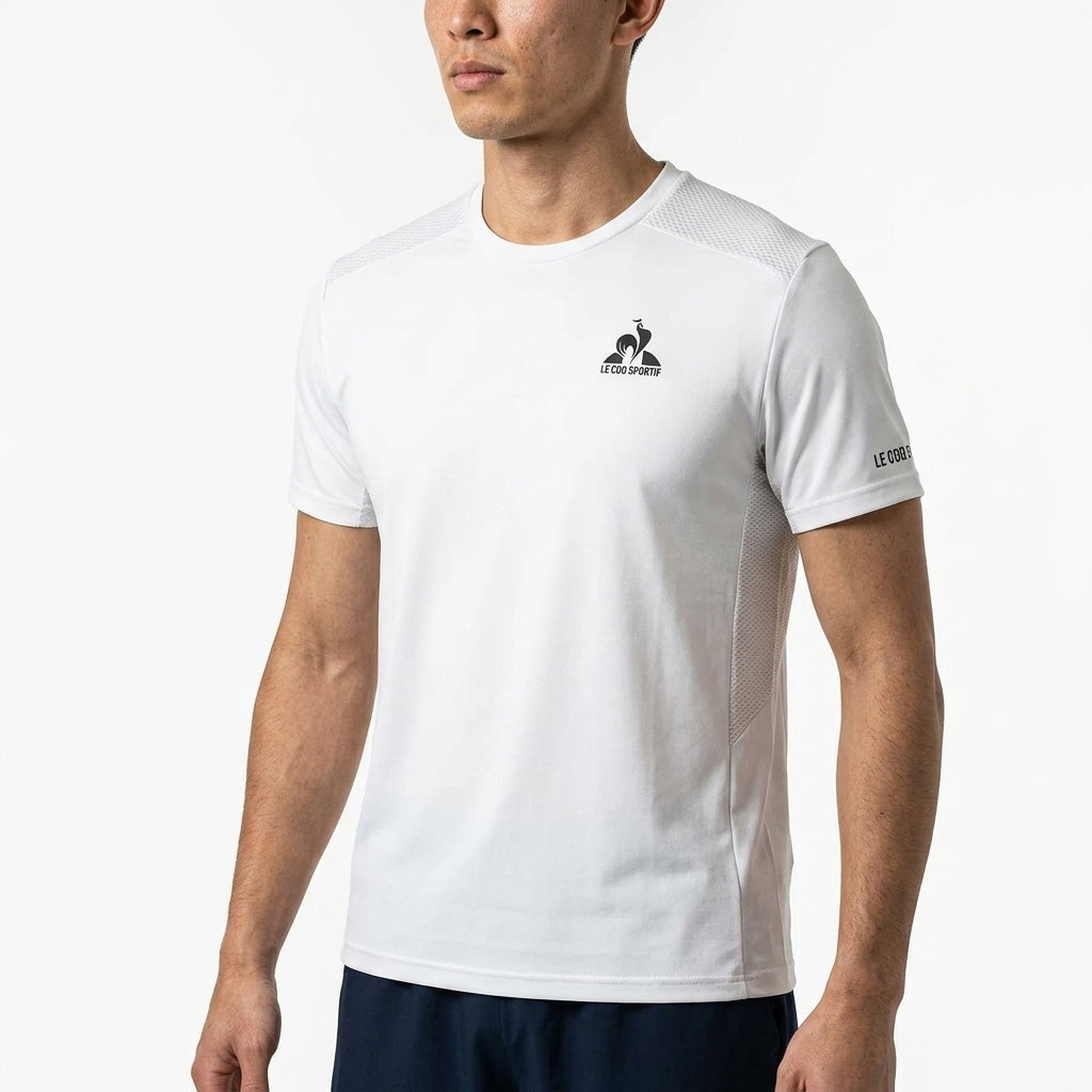A man wears the Le Coq Sportif Pro Mens Badminton T-Shirt in Optical White, featuring a small chest and left sleeve logo. He stands against a white background, with only his upper body visible, highlighting this classic Le Coq Sportif style.
