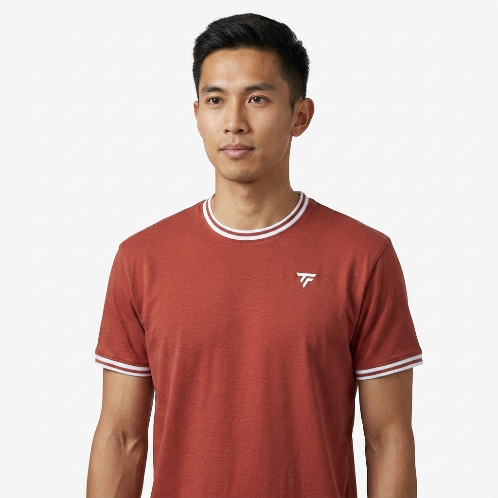 A man with short black hair wears a terracotta Tecnifibre Team Stretch Mens Badminton T-Shirt, featuring white trim and a small white logo, standing against a plain white background.