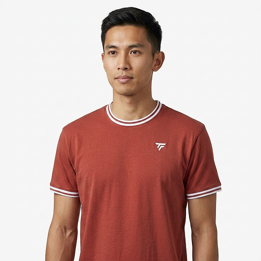 A man with short black hair wears a terracotta Tecnifibre Team Stretch Mens Badminton T-Shirt, featuring white trim and a small white logo, standing against a plain white background.