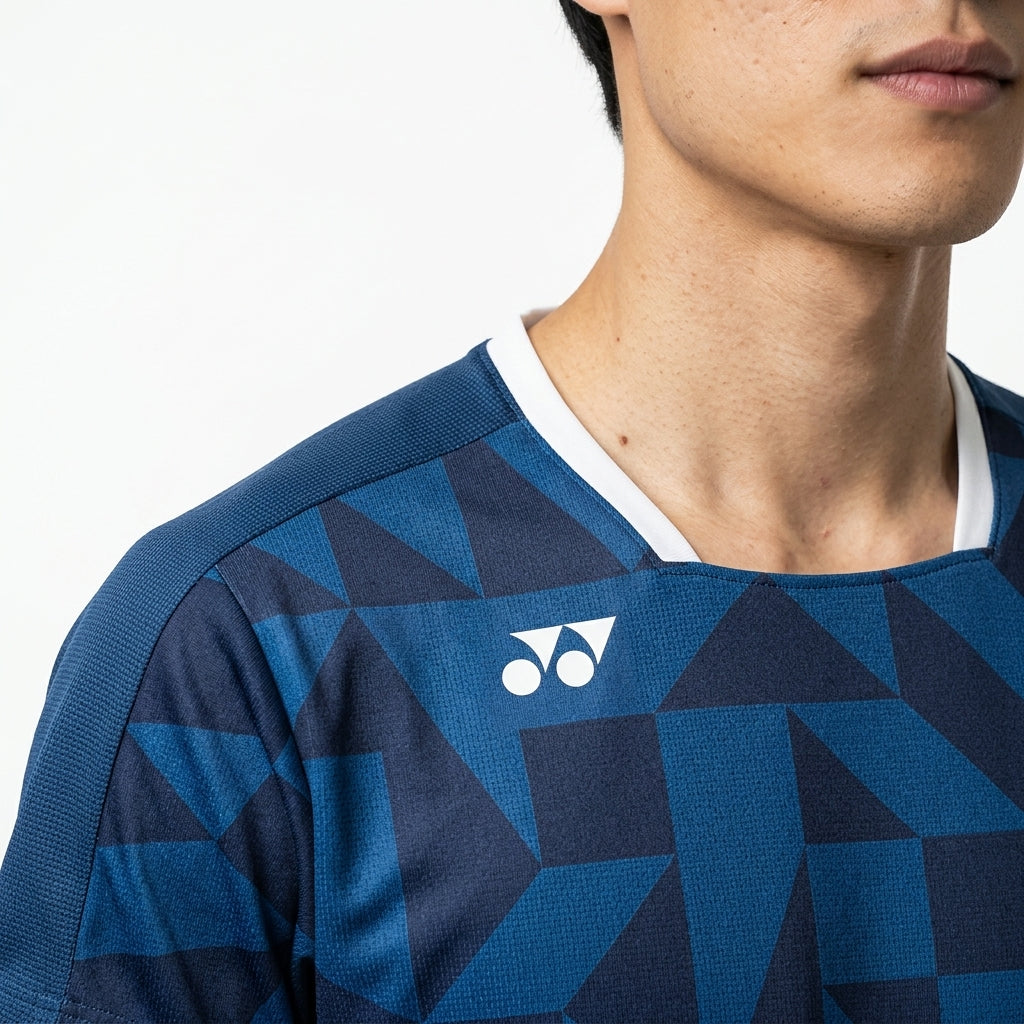 A person wearing the Yonex 10712YX Crew Neck Men's Badminton T-Shirt in indigo blue, featuring geometric patterns and a white Yonex logo on the chest, shown from the shoulders up against a plain background.
