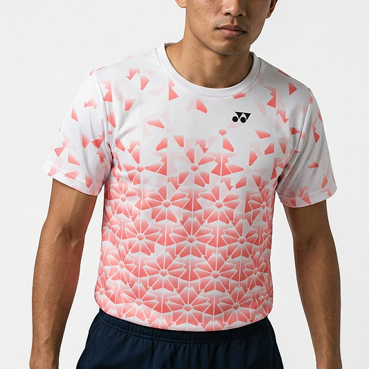 A person wears the Yonex YTM2025B Men’s Badminton T-Shirt in white, featuring a pink geometric floral pattern and small black logo, paired with dark shorts against a plain background.